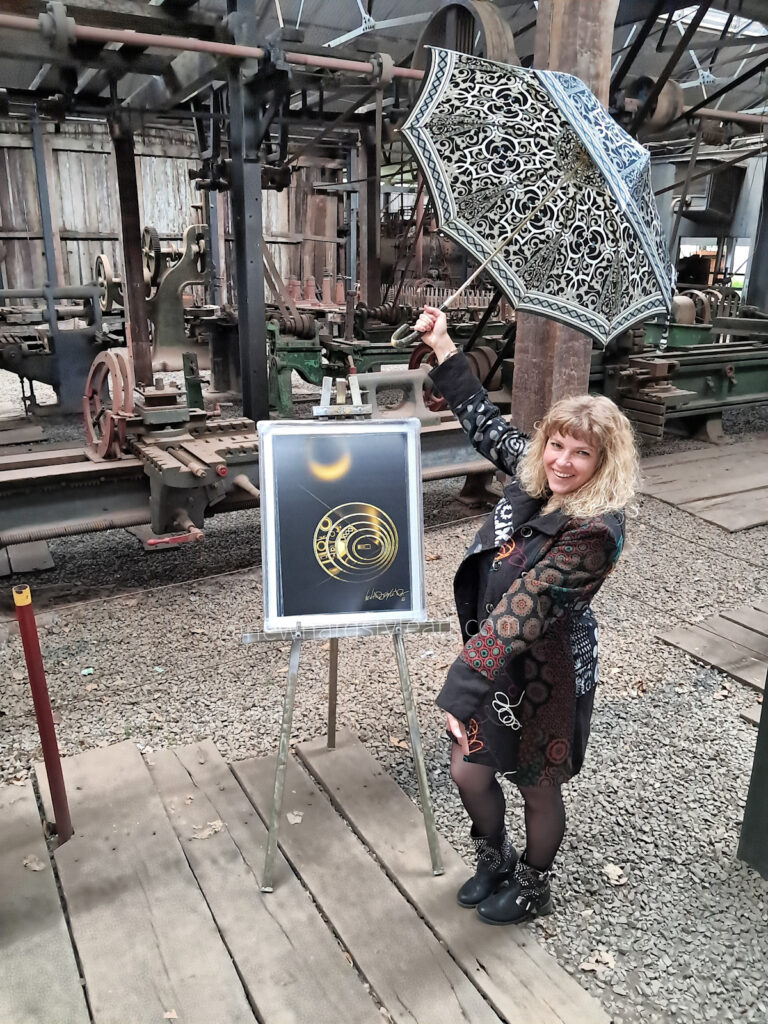 Das Bild „Goldenes Uhrwerk von Newhardstyleart®“ zeigt ein strahlend goldenes, abstraktes Design vor tiefschwarzem Hintergrund, das eine Mischung aus Mechanik und Kosmos verkörpert. Im oberen Bereich schwebt ein leuchtender, ringförmiger Kreis – wie eine Sonnenfinsternis, deren Ränder in warmem Gold erstrahlen. Darunter dominiert ein größeres, komplexes Rundmotiv, das aus mehreren konzentrischen Kreisen aufgebaut ist. Die linke Hälfte dieses Hauptkreises ist reich an geometrischen Elementen: gefüllte und hohle Kreise, feine Linien und stufenförmige Muster, die an Zahnräder, Schaltkreise oder Symbole erinnern. Die rechte Hälfte hingegen wirkt klarer und harmonischer – ein gleichmäßiger Rhythmus aus goldenen Ringen, die sich zum Zentrum hin verengen. Eine feine Diagonale durchschneidet das gesamte Rund, als würde sie zwei Welten trennen und zugleich verbinden. Unten rechts prangt die geschwungene goldene Signatur „NewHardstyleArt“. In seiner Anmutung wirkt das Werk wie eine Verschmelzung von Uhrwerk und Sonnensystem – ein Sinnbild für präzise Zeitmessung, kosmische Ordnung und das strahlende Mysterium des Universums.